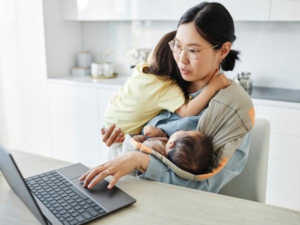 Mum nursing two children while trying to work on her laptop
