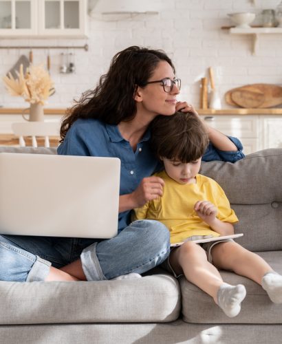 Caring mom businesswoman happy to work from home on quarantine hug son playing on digital tablet